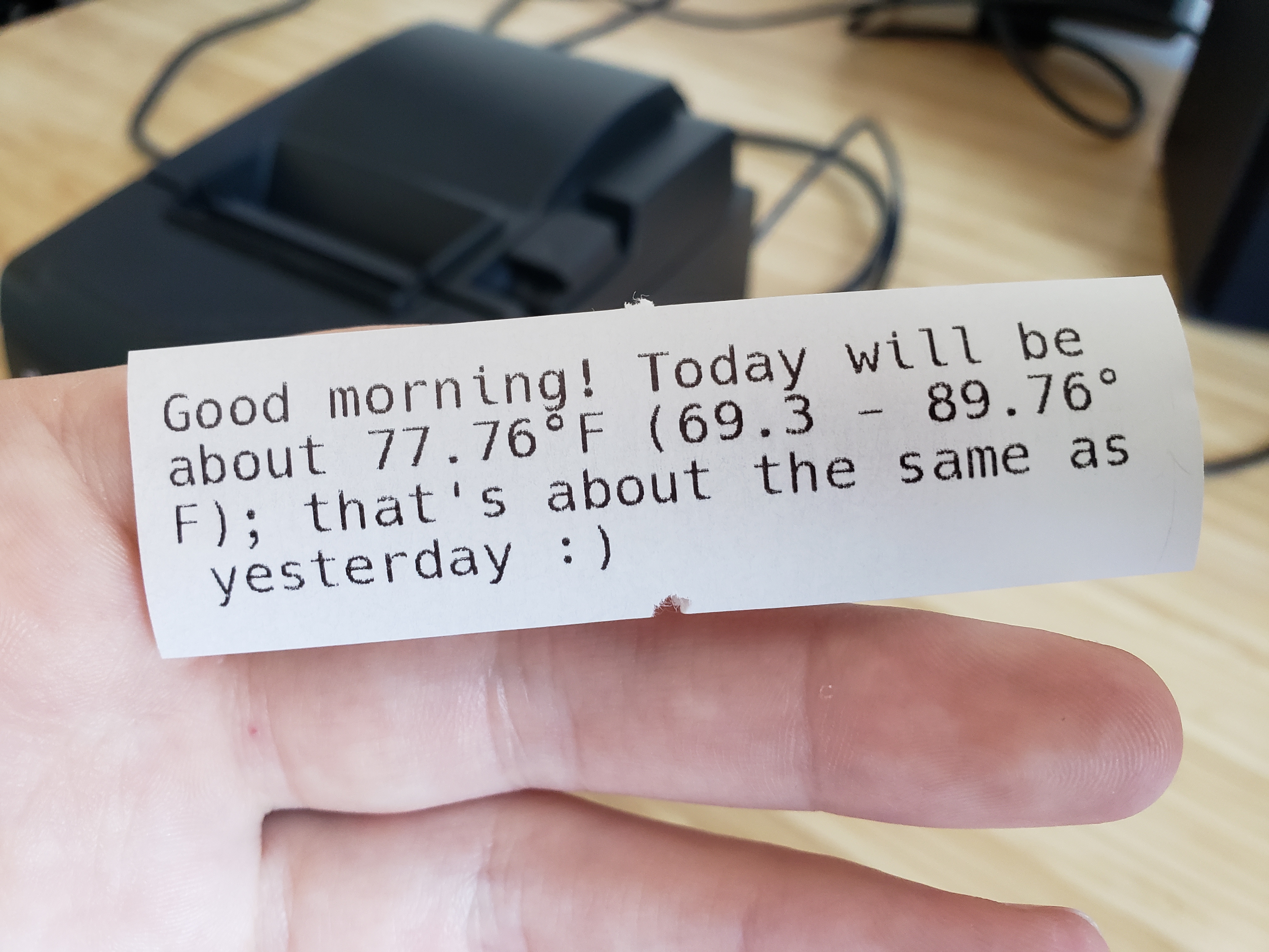 Me holding a printed receipt in my hand, which reads "Good morning! Today will be about 77.76°F (69.3 - 89.76°F); that's about the same as yesterday :)